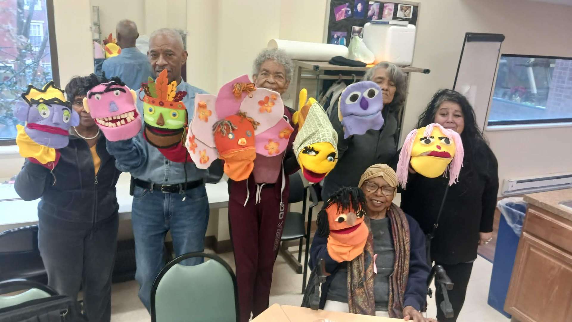 Older adults proudly display colorful handmade puppets at a creative aging workshop