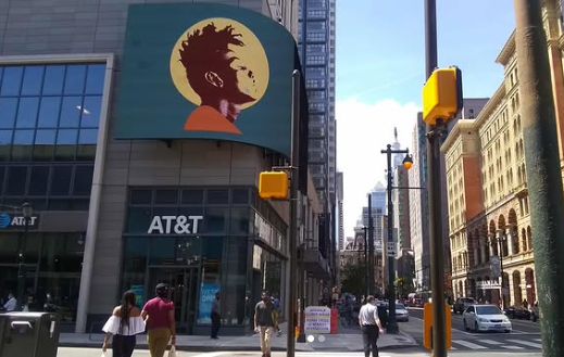 Large billboard exhibition of curated artwork above an AT&T storefront in an urban setting